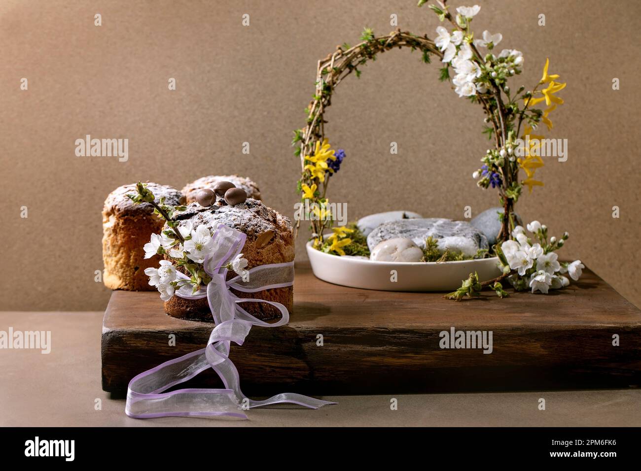 Dolci pasquali tradizionali italiani fatti in casa, decorati con uova di cioccolato, nastro rosa e fiori di ciliegio fioriti in piedi su TA di legno Foto Stock