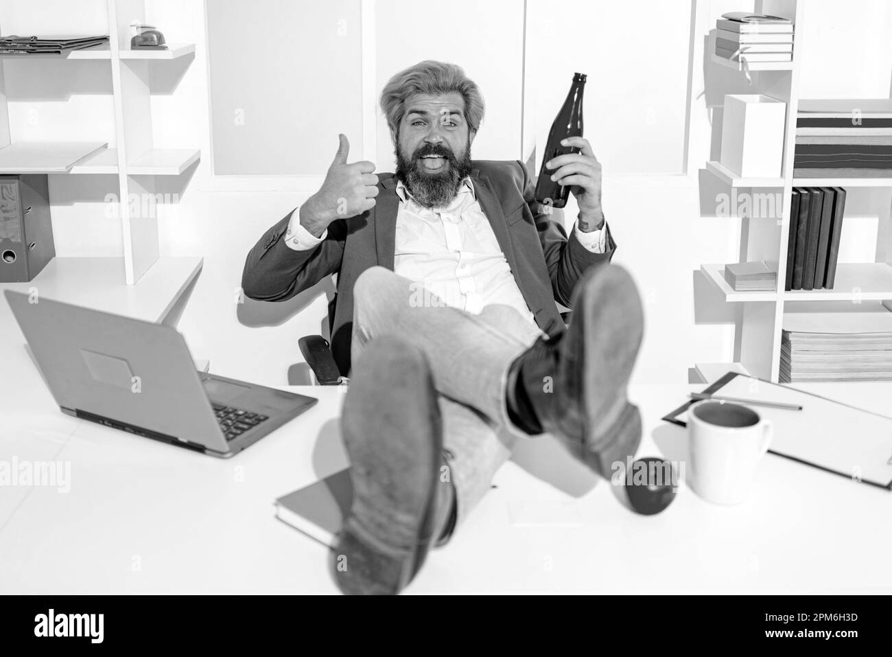 Ubriaco lavoratore in ufficio. Dipendente ubriaco bearded divertente in ufficio. Buon lavoratore con una bottiglia di birra. Foto Stock