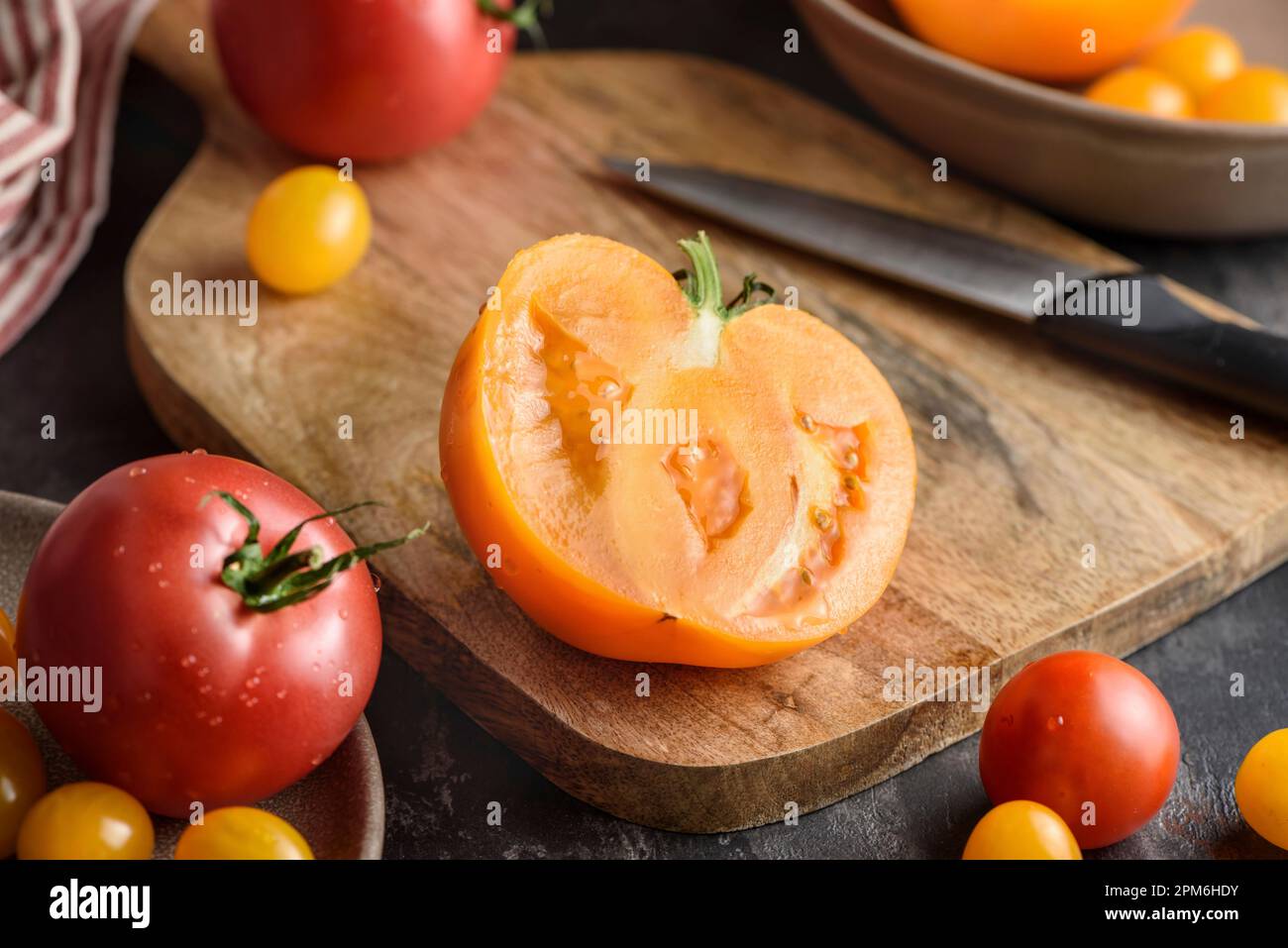 Mezzo pomodoro su un tagliere. Nelle vicinanze ci sono vari pomodori gialli e rossi. Foto Stock