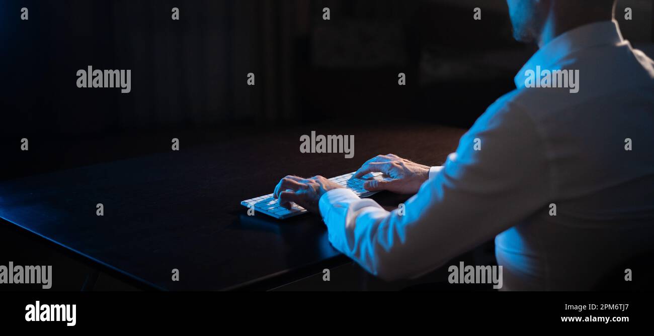 Vista posteriore di un uomo che scrive su una tastiera al buio. Foto Stock