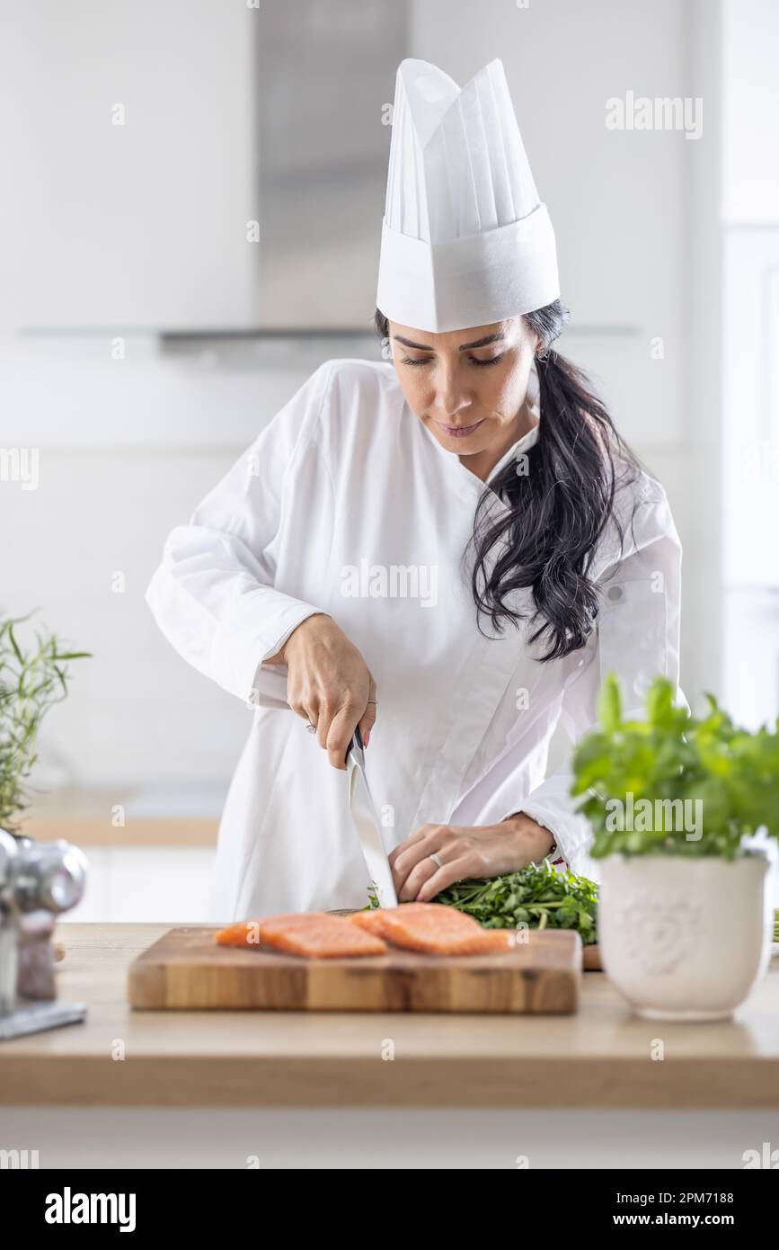 Professione di cuoco femminile al lavoro come donna in uniforme e cappello  bianco taglia il salmone su una tavola di legno in una cucina professionale  Foto stock - Alamy