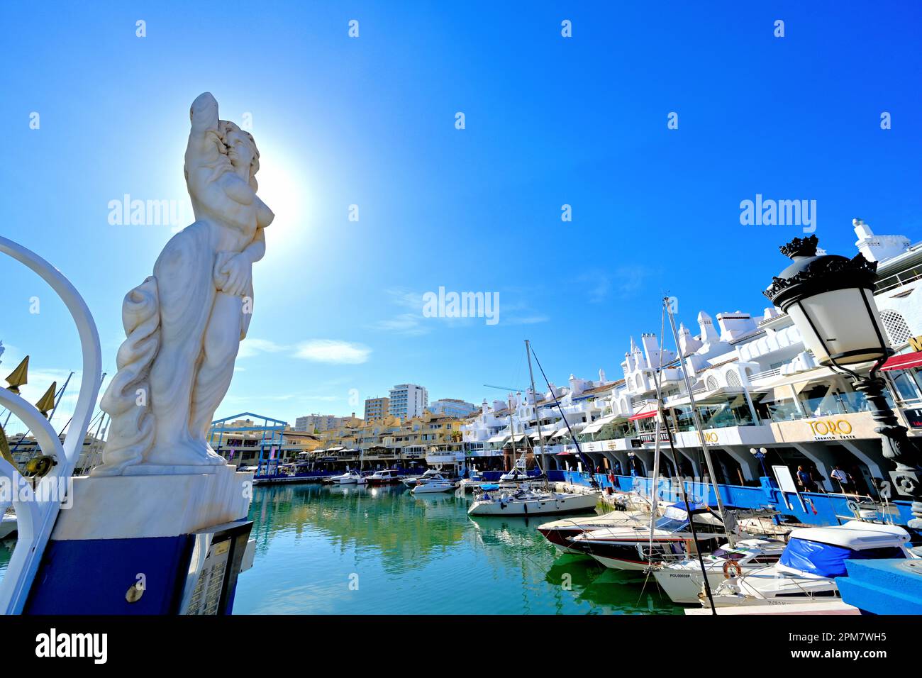 Malaga Benalmadena Marina mostra edifici bianchi con yacht e bar e una statua femminile all'ingresso contro un cielo blu profondo Foto Stock
