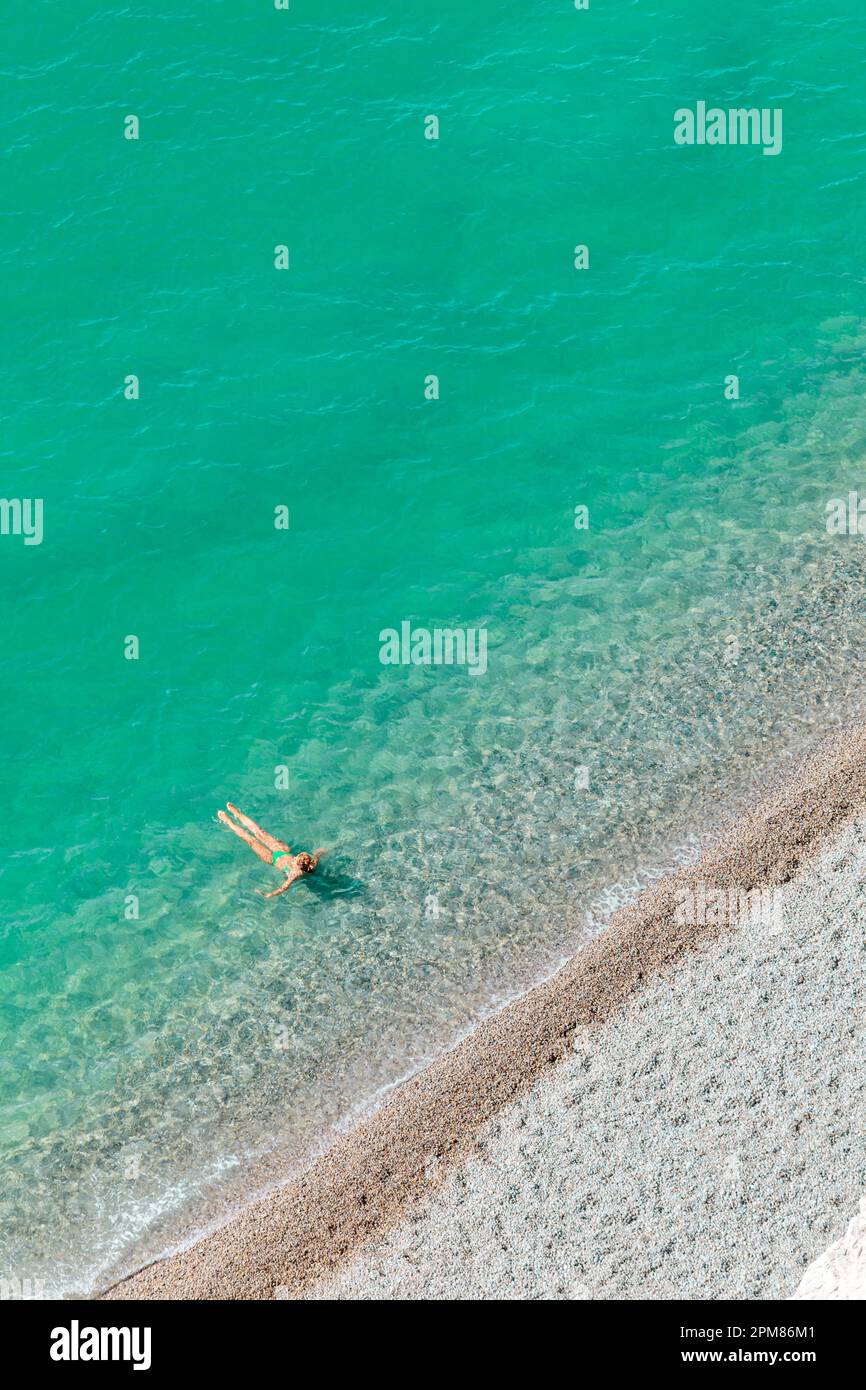 Francia, Seine-Maritime, Pays de Caux, Costa d'Alabastro (Cote d'Albatre), Etretat, Falaise d'Amont, vista dall'alto di una donna che indossa un bikini, godendo di un bagno rinfrescante in un mare turchese e trasparente, ai margini della spiaggia di ciottoli Foto Stock