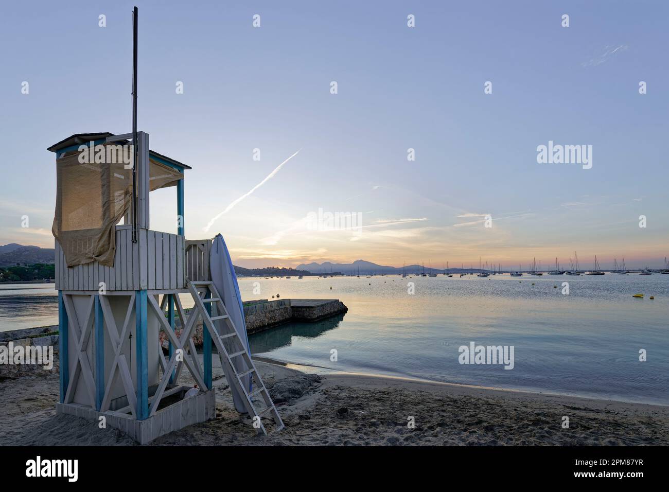 Spagna, Isole Baleari, Maiorca, Pollenza, Port de Pollenza, Cabina bagnino sulla spiaggia all'alba, sullo sfondo la baia di Pollenc e le sue barche Foto Stock