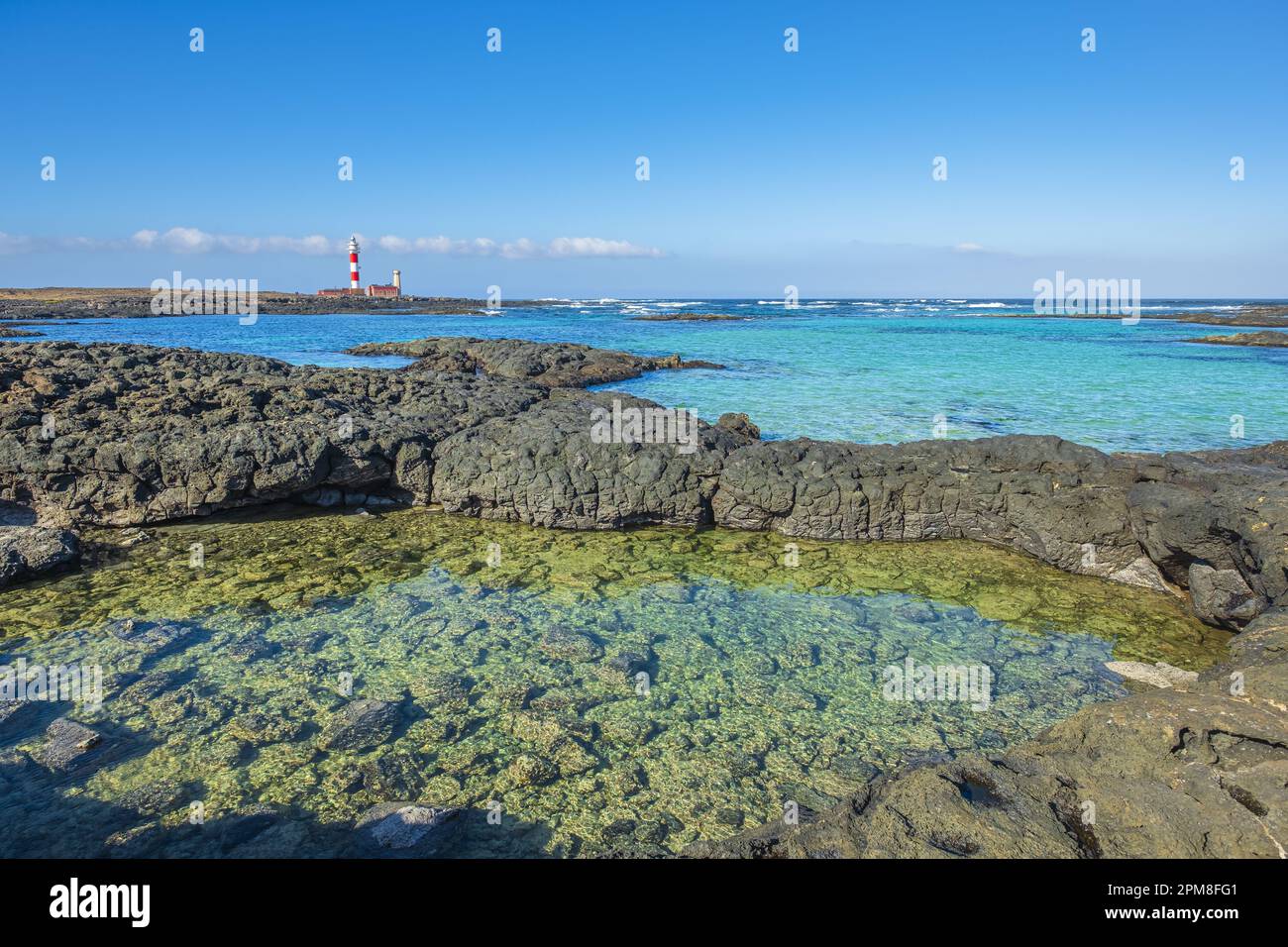 Spagna, Isole Canarie, Fuerteventura, El Cotillo, insenatura e piscine naturali della Caleta del Marrajo, faro di Toston a Punta de la Ballena sullo sfondo Foto Stock