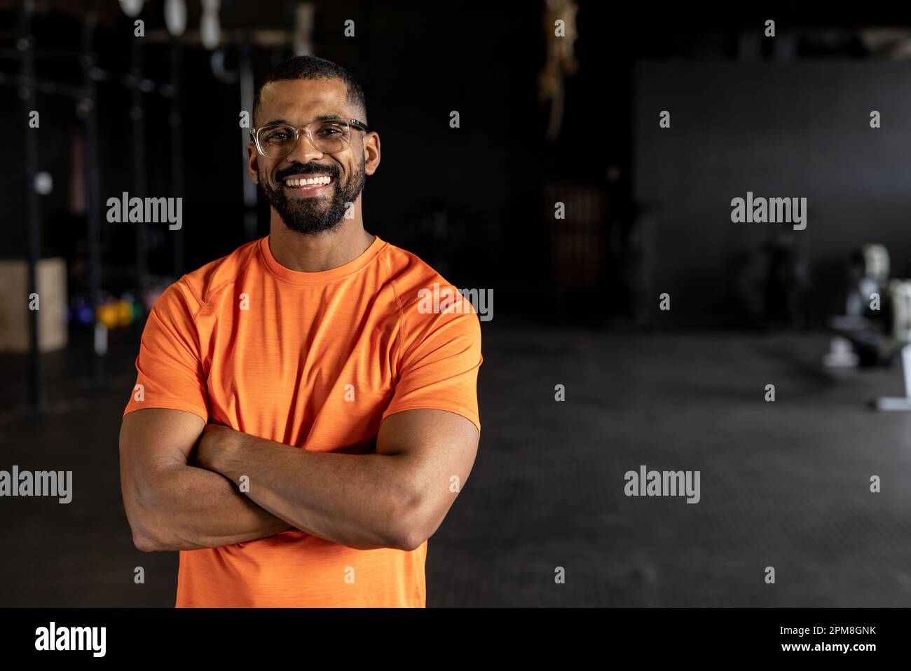 Ritratto di giovane beared biracial con le braccia incrociate sorridendo e in piedi in palestra Foto Stock