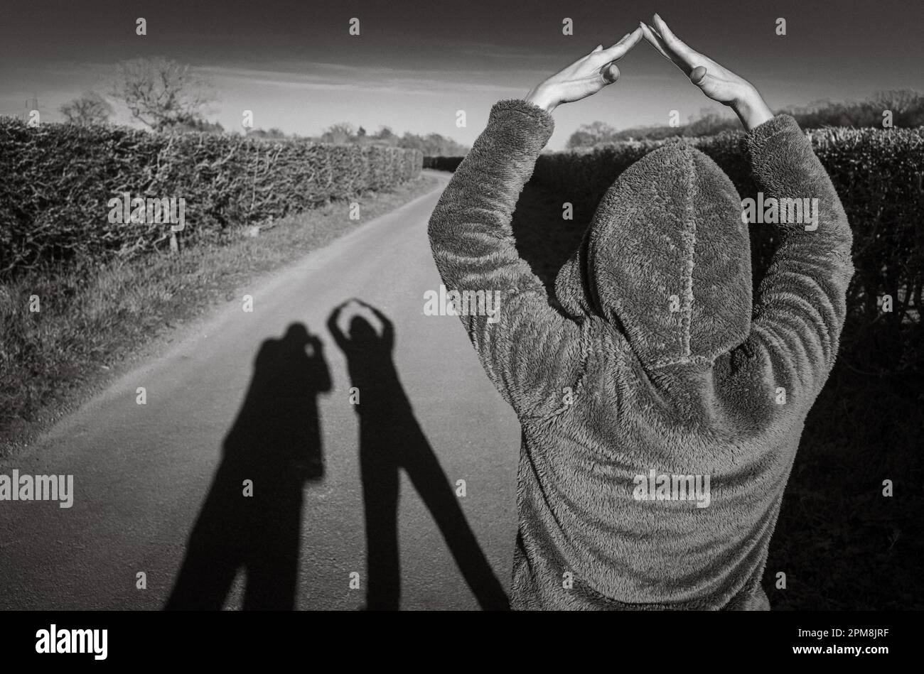 Una donna colpisce una posa per formare ombre allungate di una coppia mentre camminano lungo una corsia di campagna a Billingshurst, West Sussex, UK, la sera. Foto Stock