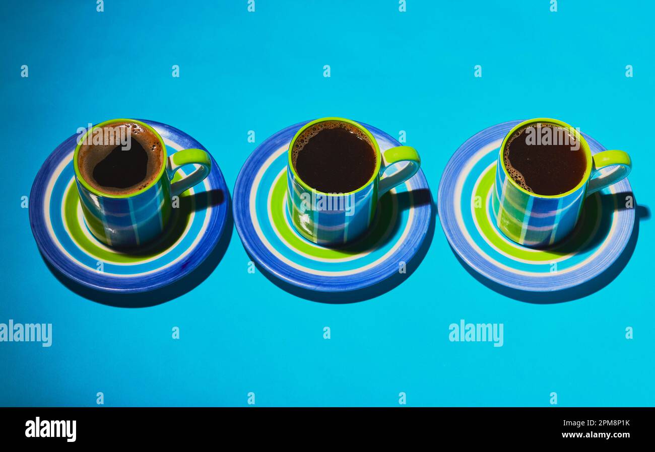 Tre tazze di caffè con piattini su sfondo blu. Foto Stock