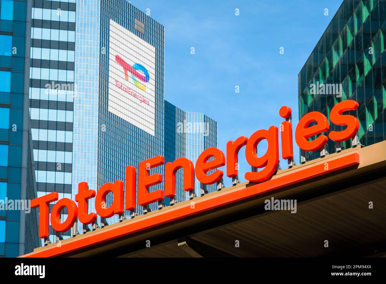 Segno di una stazione di servizio TotalEnergies con la torre Coupole sullo sfondo, sede della compagnia petrolifera nel quartiere finanziario di Parigi la Defense Foto Stock