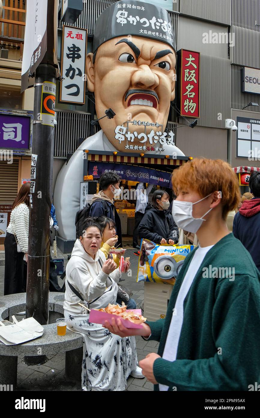 Osaka, Giappone - 21 marzo 2023: Persone che mangiano cibo di strada nel quartiere Dotonbori di Osaka, Giappone. Foto Stock