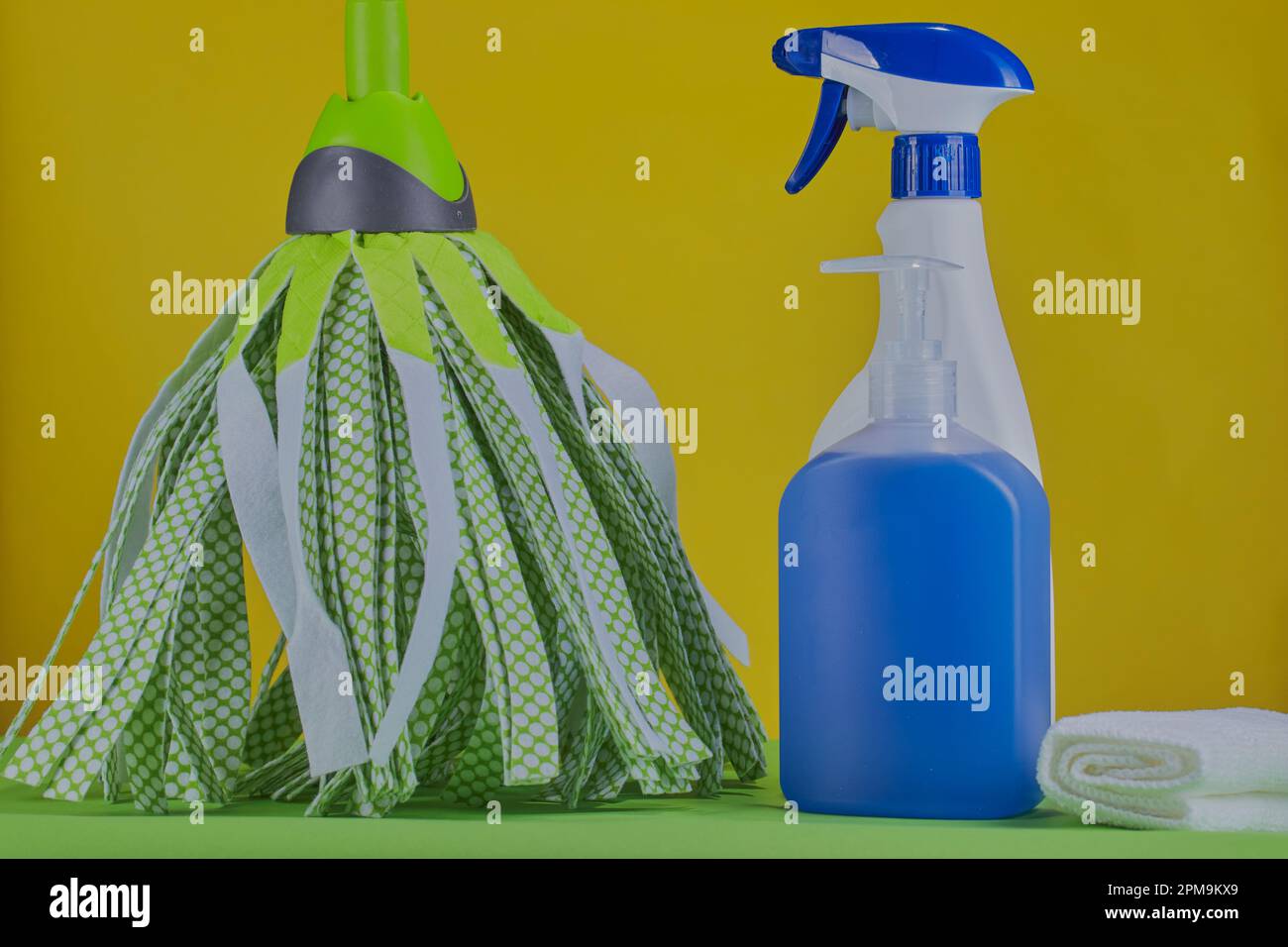 Prodotti per la pulizia un mop e uno spray per la pulizia su sfondo giallo brillante. Foto Stock