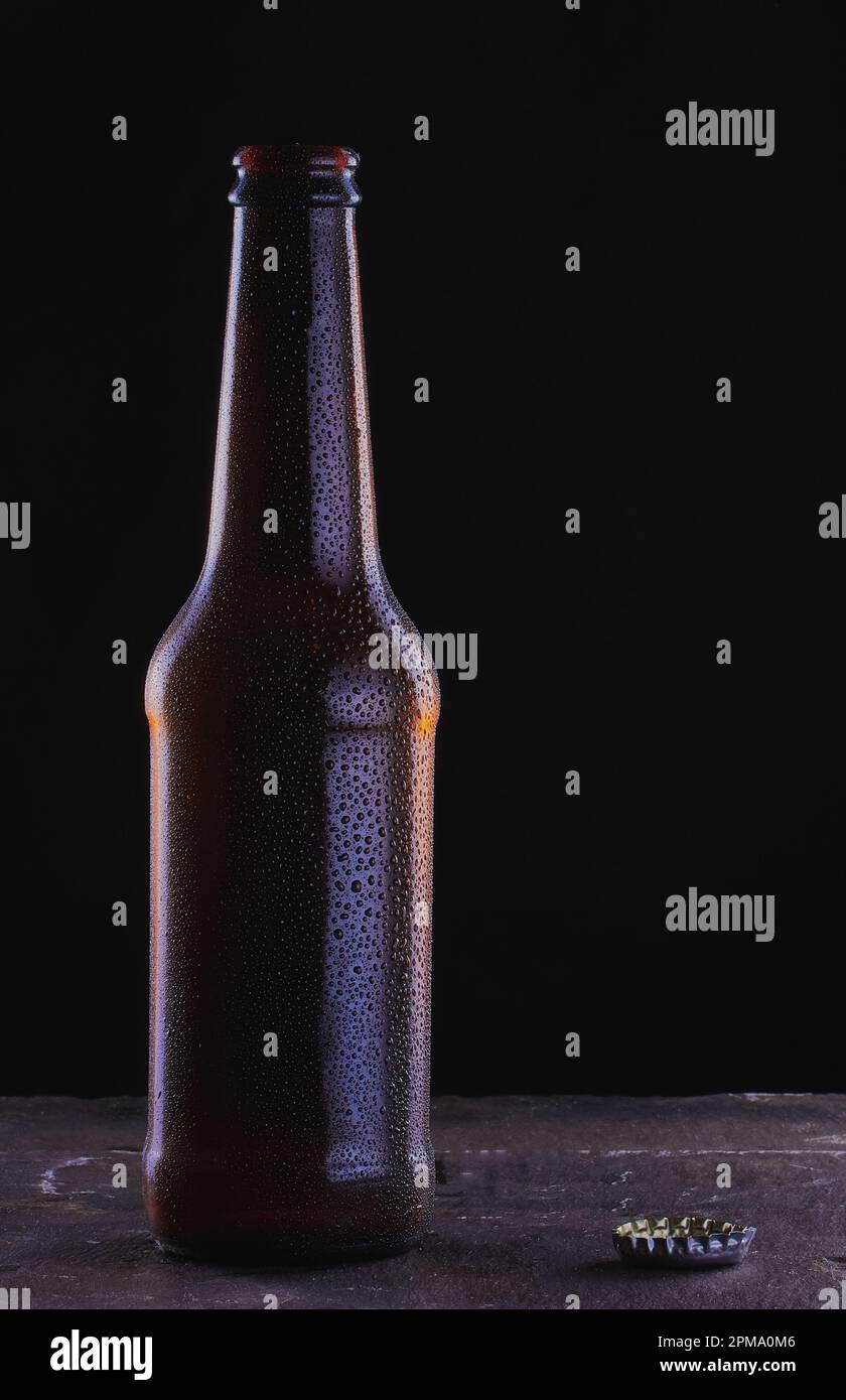 Bottiglia di birra fredda su una superficie ardesia e fondo nero con gocce sulla bottiglia. Foto Stock