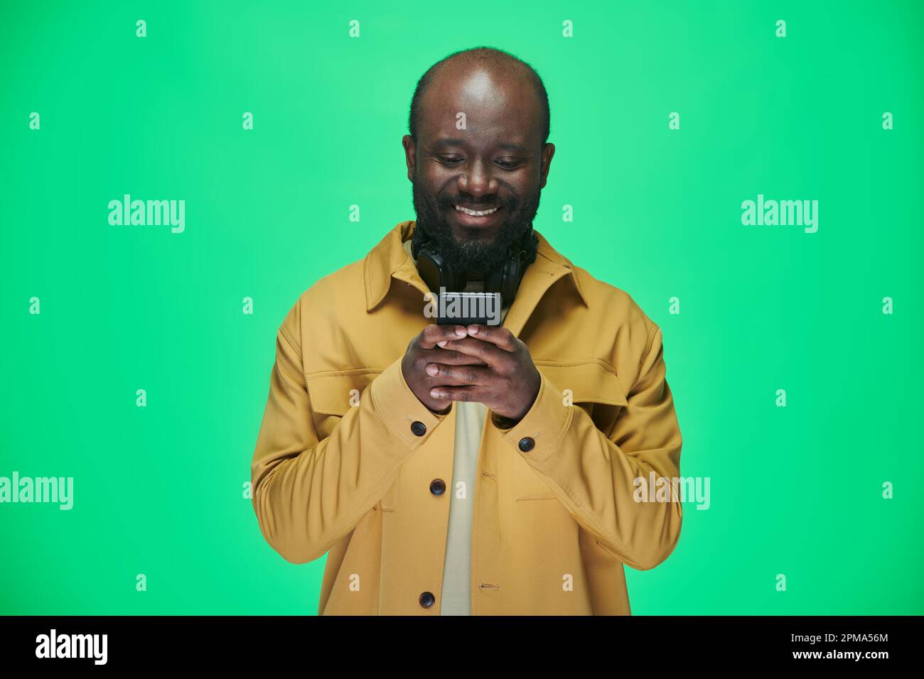 L'uomo afroamericano legge un messaggio sul suo cellulare e sorridendo in piedi contro lo sfondo verde Foto Stock