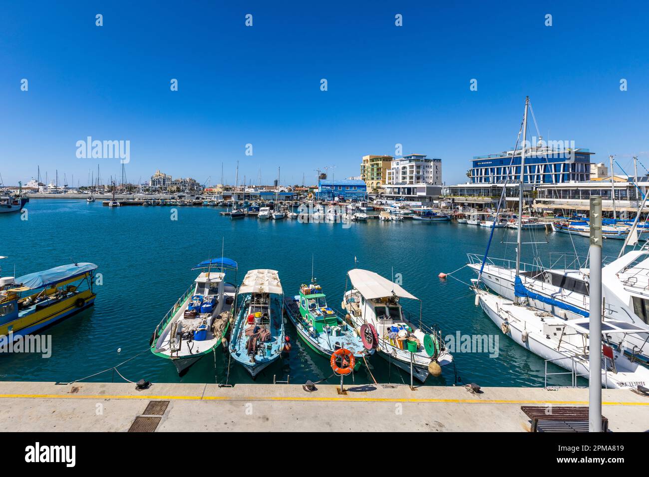 Barche da pesca colorate sono ormeggiate nel Vecchio Porto di Limassol, Cipro, sullo sfondo della marina adiacente con yacht a vela e nuovi edifici a più piani. Foto Stock