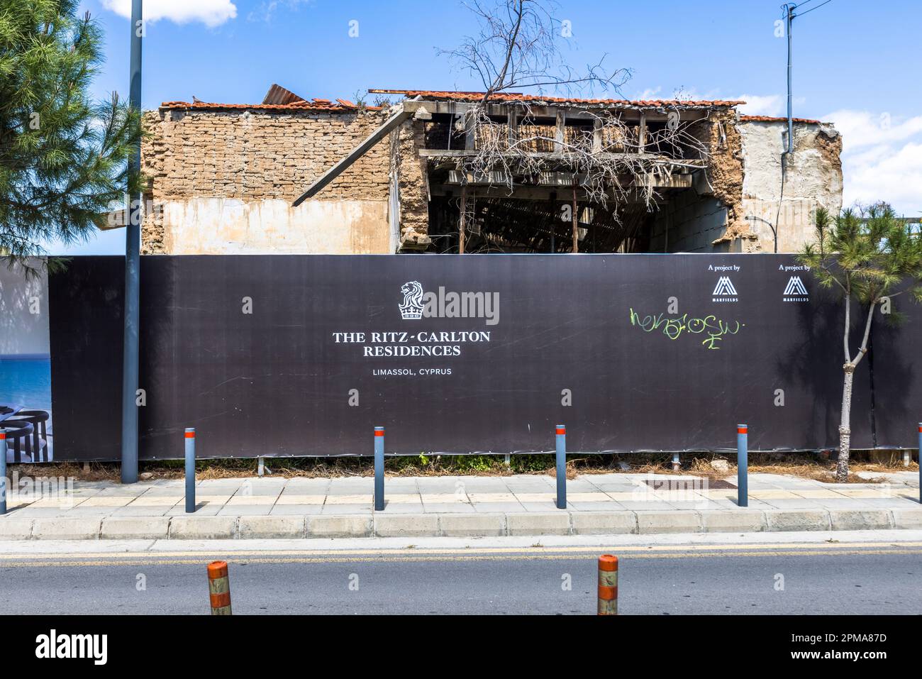 Le travi del tetto collassate di una casa in pietra abbandonata si ergono dietro un cartello di cantiere che annuncia "The Ritz-Carlton Residences" a Limassol, Cipro. L’hotel e la torre residenziale, progettati dal gruppo Ritz-Carlton con circa 33 piani, dovevano essere originariamente completati nel 2022 secondo lo sviluppatore. Foto Stock