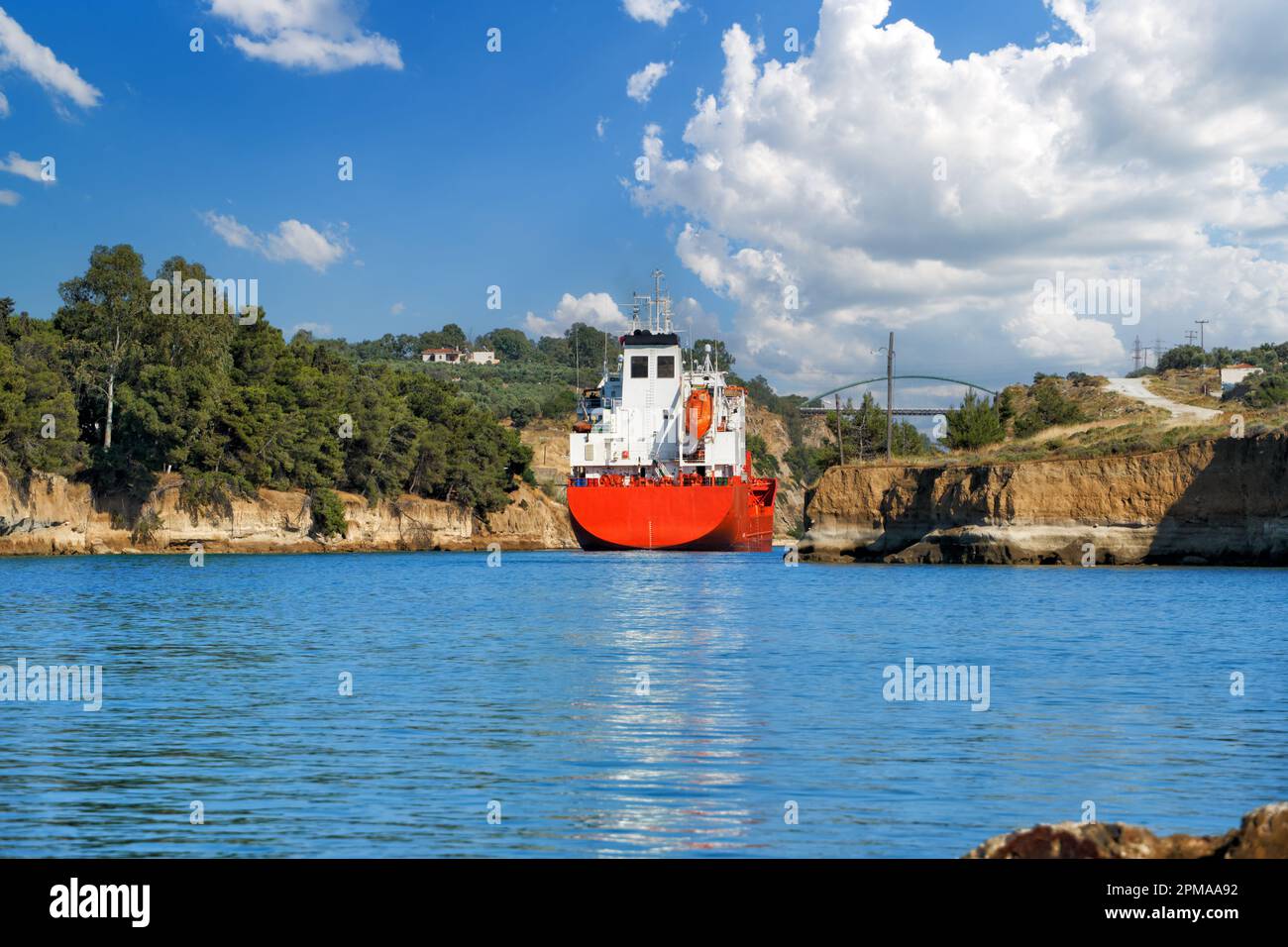 La petroliera naviga tra le rocce del canale di Corinto. Paesaggio estivo panoramico del canale di Corinto in una giornata di sole luminoso contro un cielo blu con bianco Foto Stock
