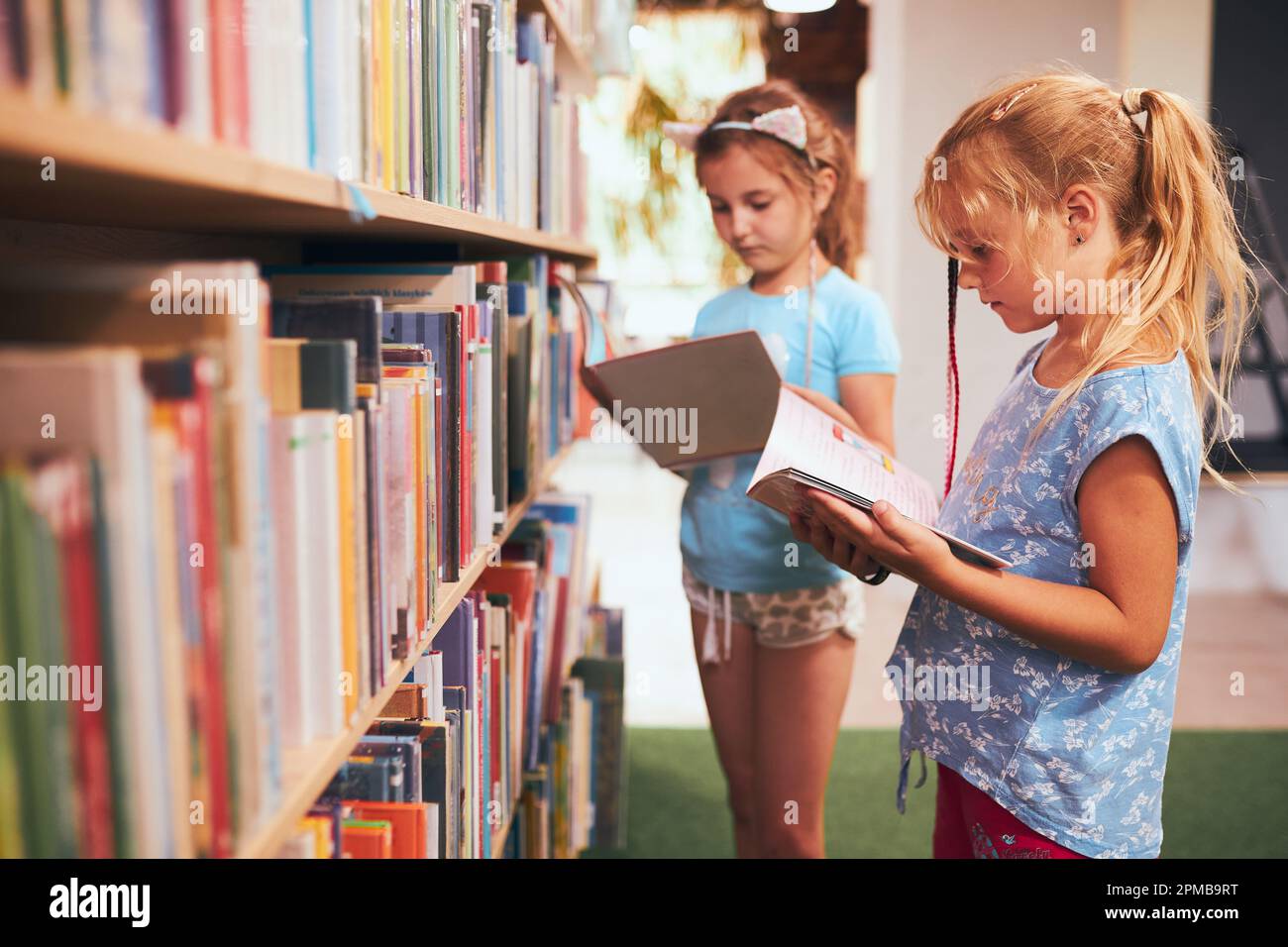 Due scolaresche che scelgono libri nella biblioteca scolastica. Studenti della scuola elementare che imparano dai libri. I bambini si divertono nel club scolastico. Ritorno a scuola. Doi Foto Stock