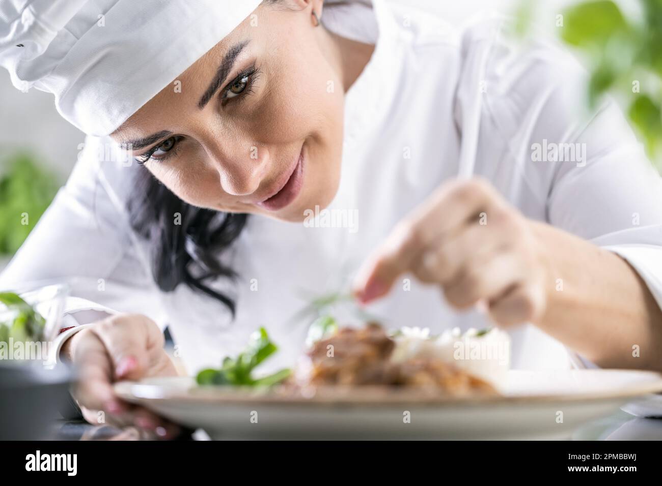 Una giovane cuoca femminile finisce il pasto con erbe nella cucina del ristorante - primo piano. Foto Stock