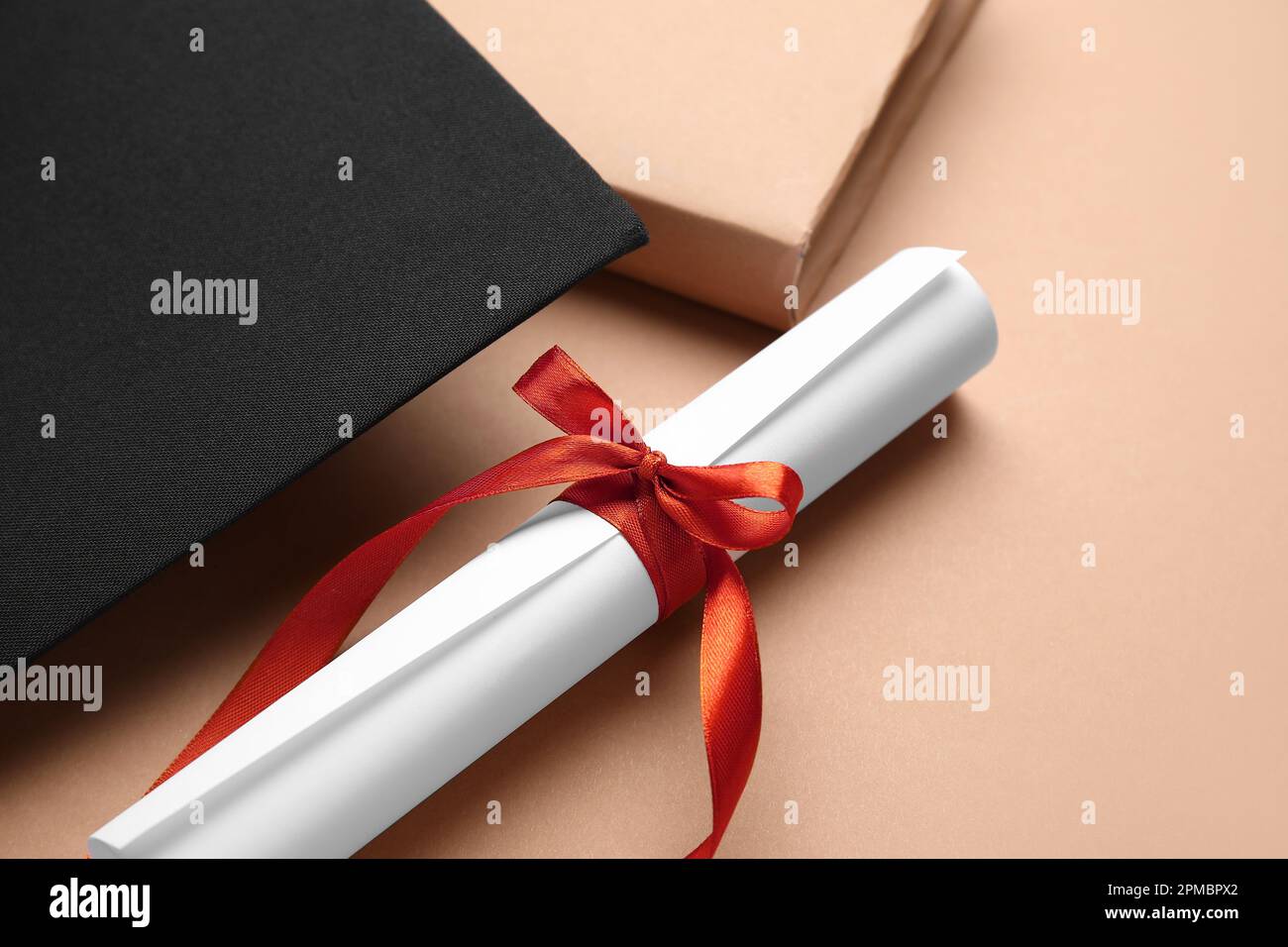 Diploma con nastro rosso, cappello di laurea e libro su sfondo marrone Foto Stock