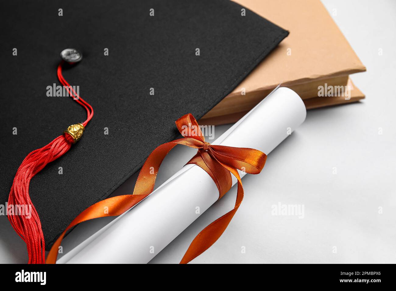 Diploma con nastro rosso, cappello di laurea e libro su sfondo bianco Foto Stock