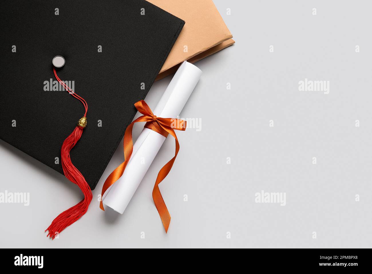 Diploma con nastro rosso, cappello di laurea e libro su sfondo bianco Foto Stock