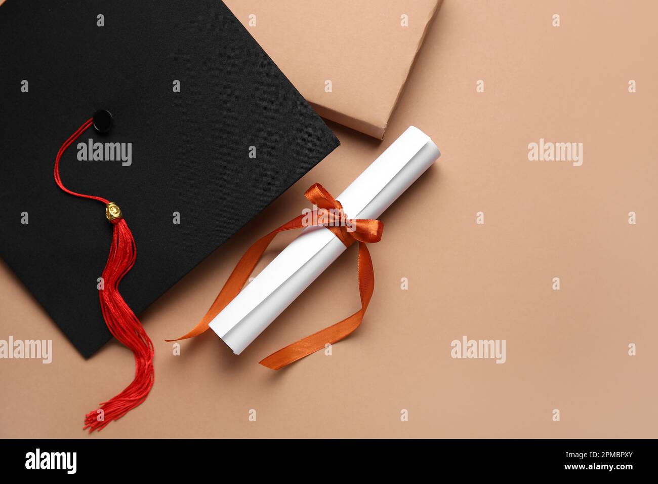 Diploma con nastro rosso, cappello di laurea e libro su sfondo marrone Foto Stock