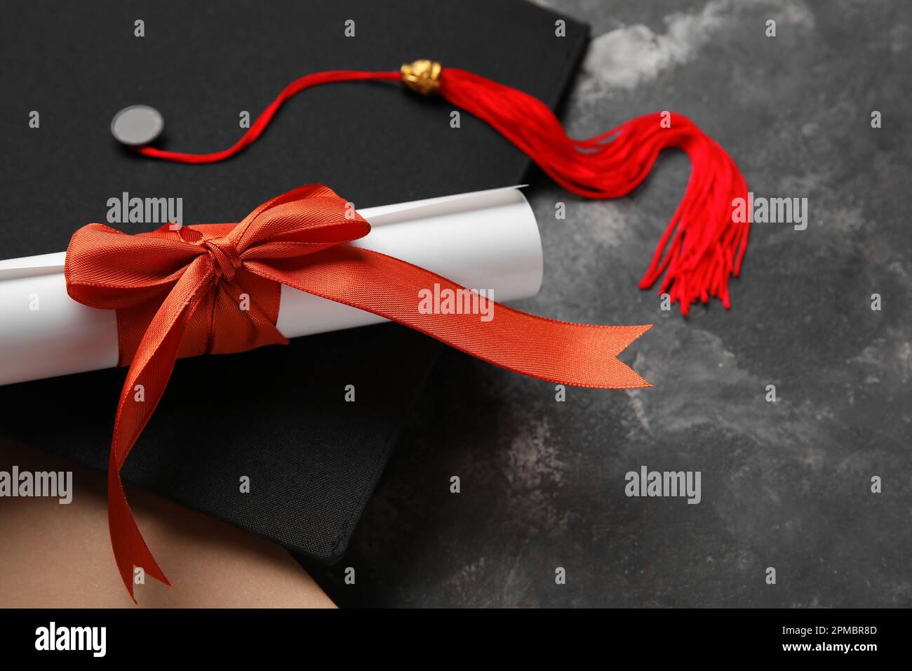 Diploma con nastro rosso, cappello di laurea e libro su tavolo grigio scuro Foto Stock