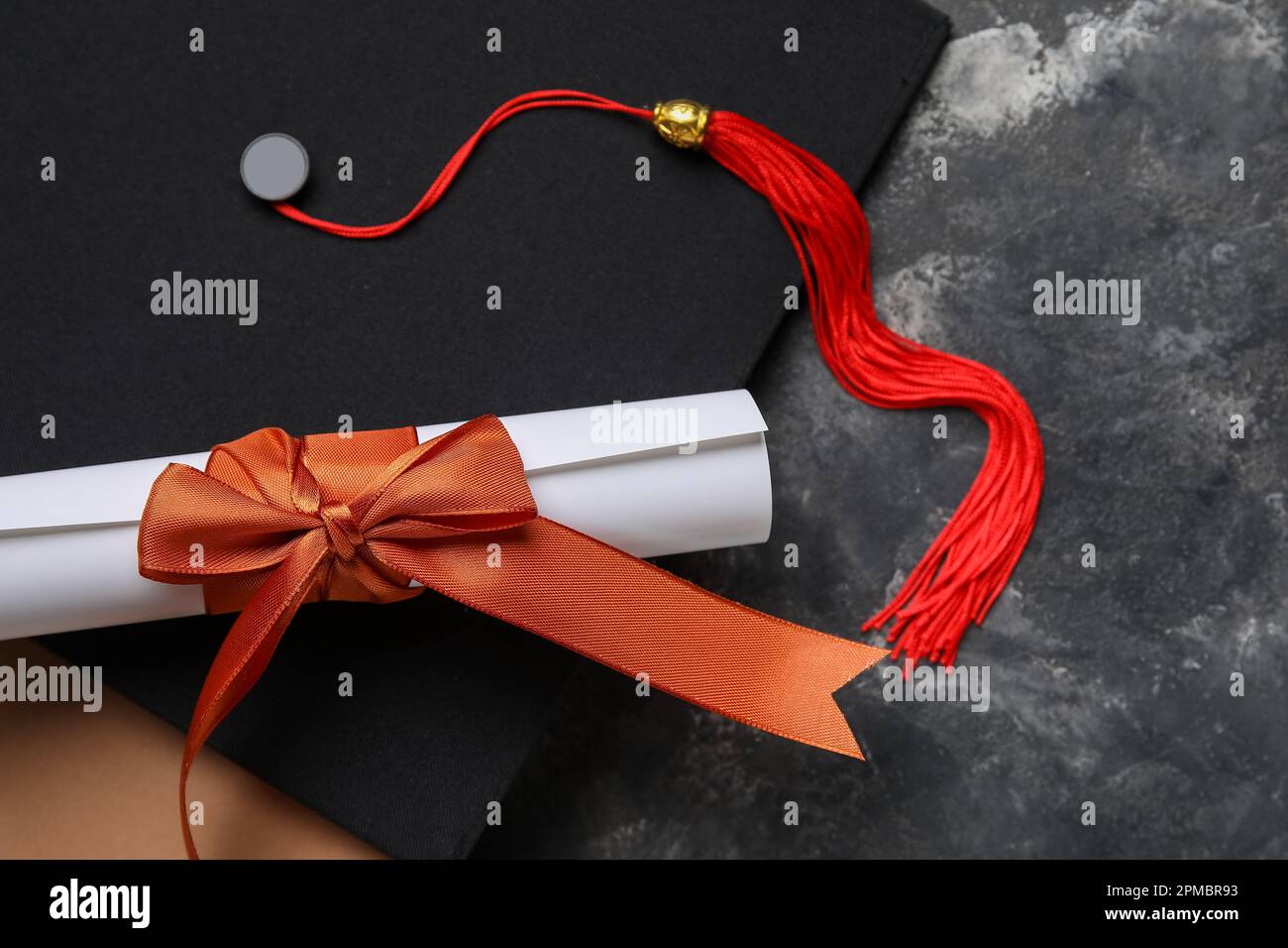 Diploma con nastro rosso, cappello di laurea e libro su tavolo grigio scuro Foto Stock