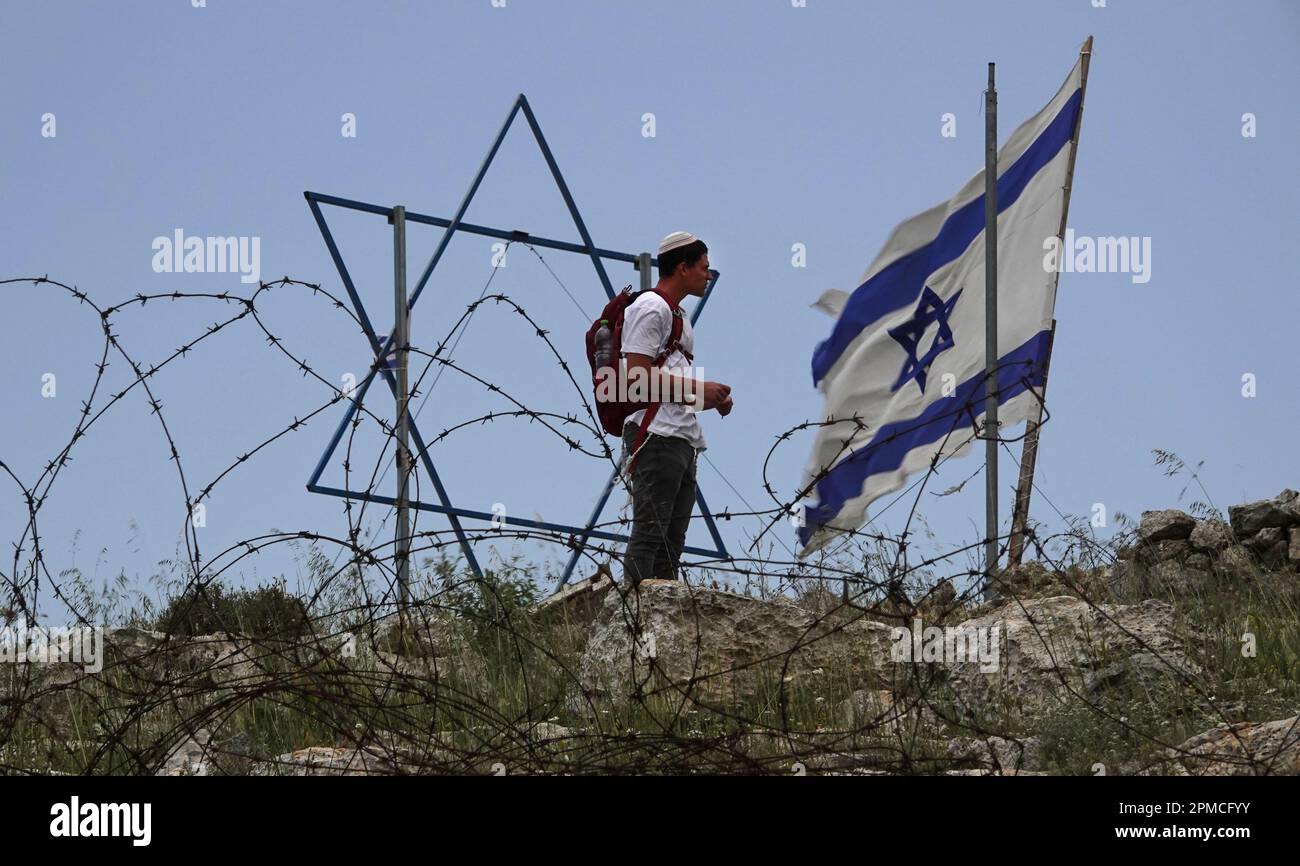 CISGIORDANIA, ISRAELE - APRILE 10: Un colono israeliano si trova accanto a una stella gigante di David e a una bandiera nazionale nell'avamposto illegale dei coloni israeliani della Cisgiordania di Evyatar dopo aver partecipato a una marcia di massa da Tapuach Junction verso Evyatar chiedendo la legalizzazione di Evyatar e di denunciare i crescenti attacchi terroristici Insediamenti nelle ultime settimane il 10 aprile 2023 in Cisgiordania, Israele. Foto Stock