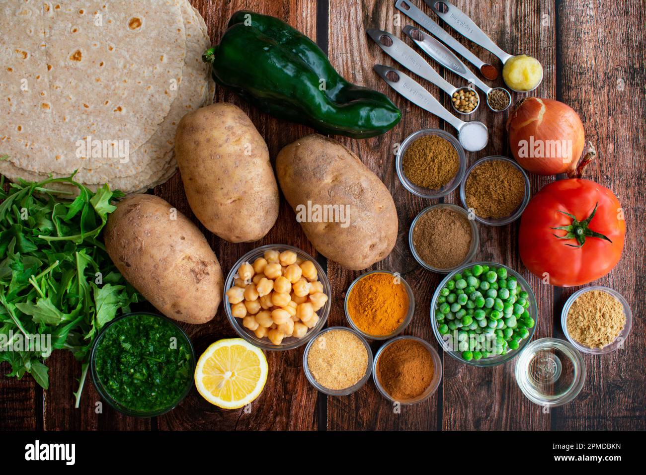 Samosa Wrap ingredienti disposti su un tavolo di legno: Patate Russet, piselli congelati, e altri ingredienti per burritos di fusione indiana Foto Stock
