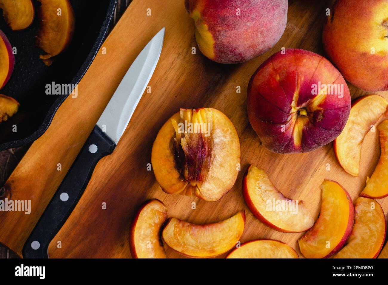 Pesche fresche tagliate a fette su un tagliere di legno: Pesche non pelate tagliate a fette sottili con un coltello da parare Foto Stock
