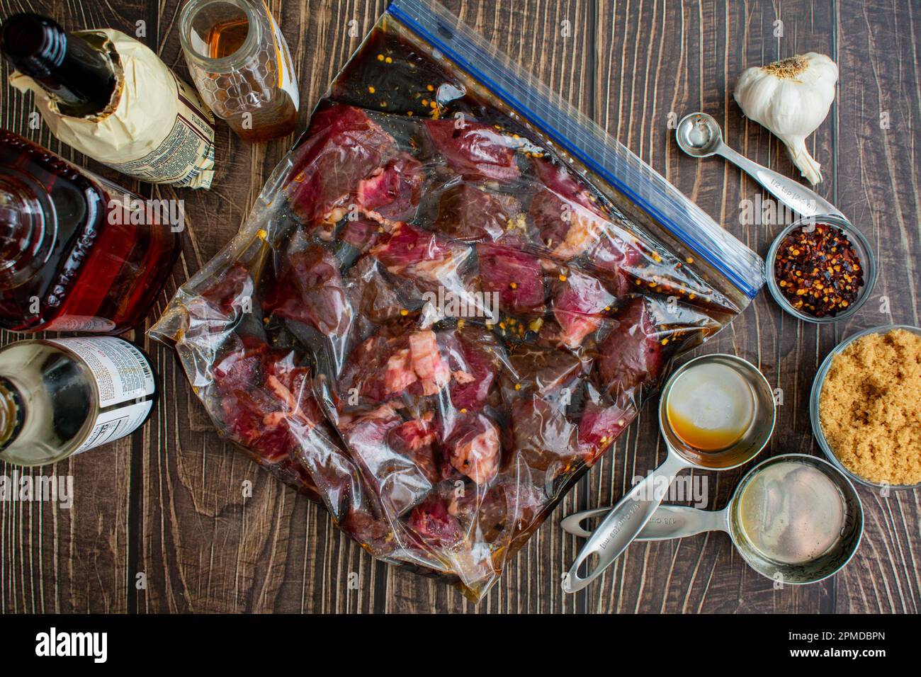 Marinare le punte di bistecca crude in un sacchetto di plastica con chiusura a cerniera: Punte di manzo crude in un sacchetto di plastica circondato da ingredienti di marinata Foto Stock