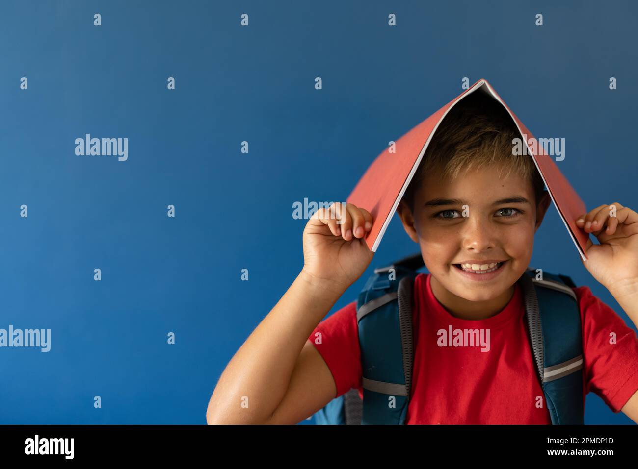 Ritratto di giocoso ragazzo caucasico con libro in testa in piedi su sfondo blu, copia spazio Foto Stock