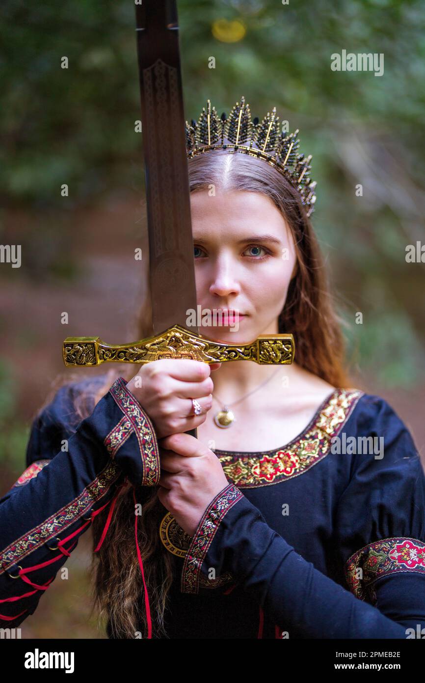 Giovane donna in costume da favola Regina con corona che avvolge la grande Broadsword | toni caldi Foto Stock