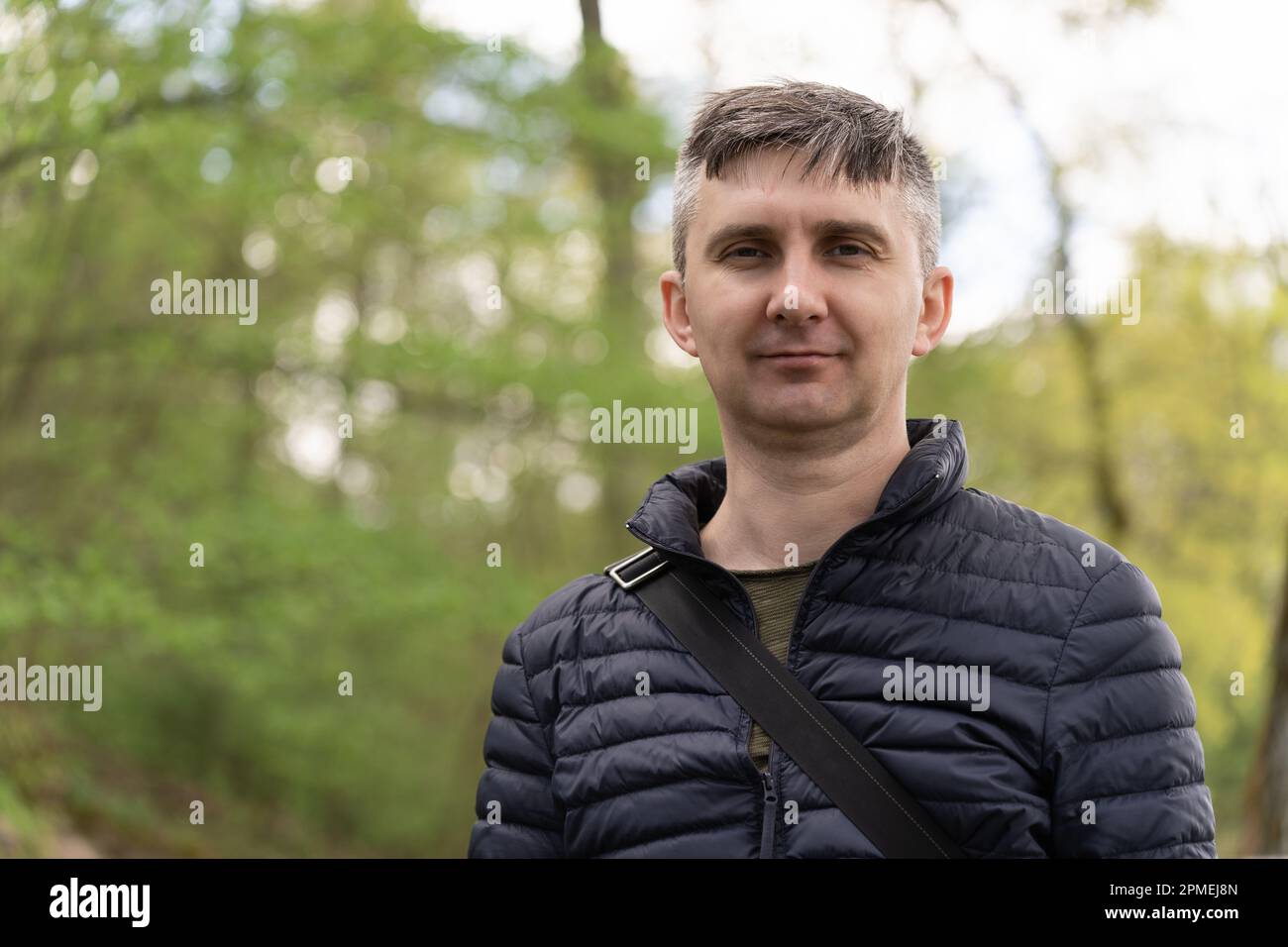 Un uomo di mezza età su uno sfondo sfocato della prima primavera verde guardando la fotocamera Foto Stock