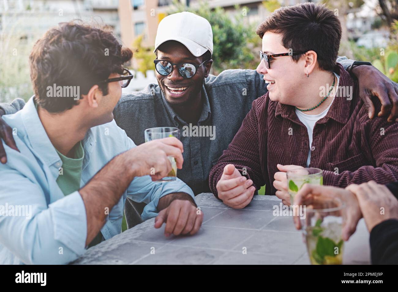 Un gruppo di giovani amici, tra cui un uomo caucasico, una persona non binaria più-taglia con capelli corti e piercing naso, e una persona africana, che chiacchiera Foto Stock
