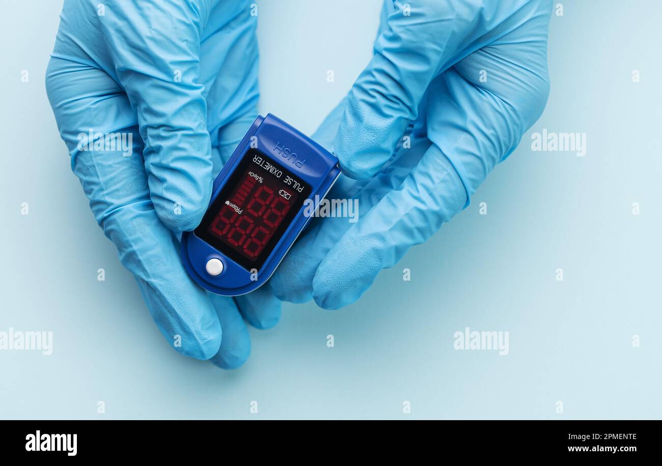 Pulsossimetro in mano del medico con guanto su sfondo blu. Una mano in un guanto medico contiene un dispositivo per la diagnostica sanitaria Foto Stock