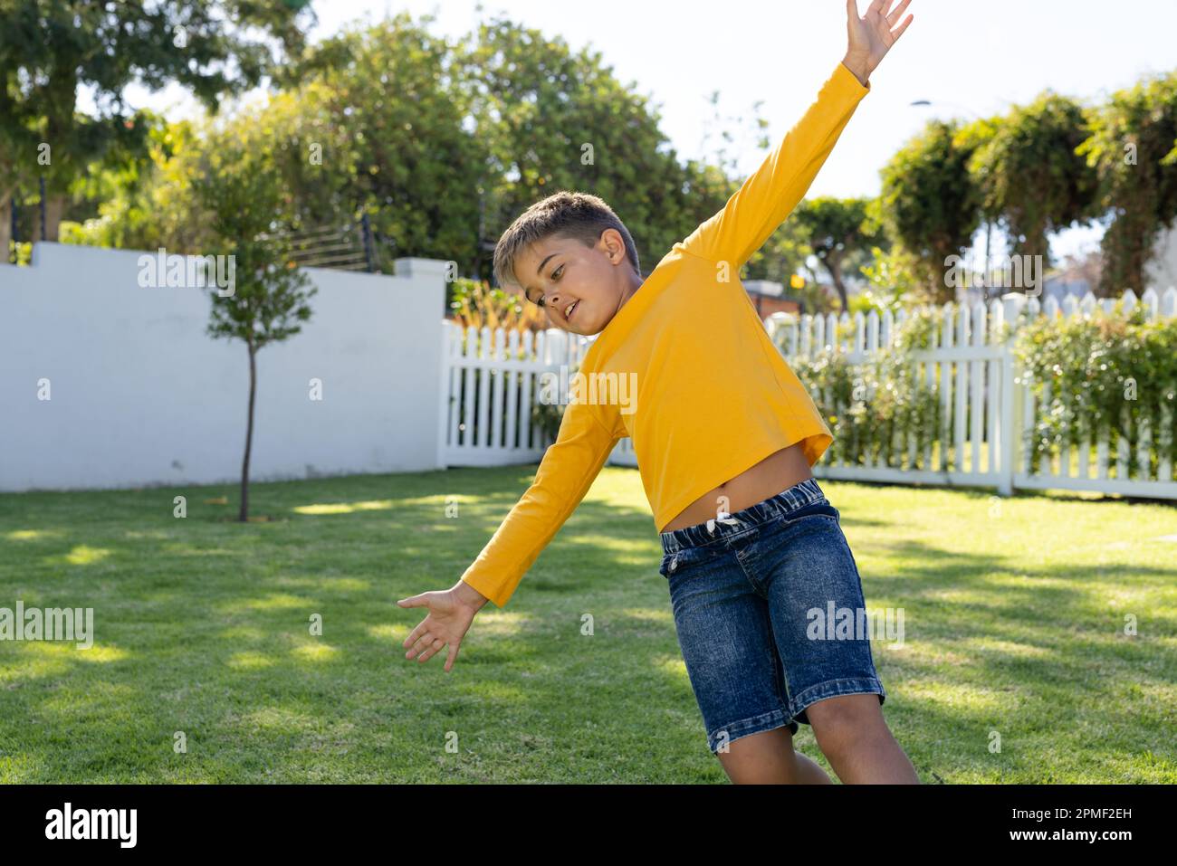 Giocoso ragazzo caucasico con braccia tese che si inclina su terra erbosa in cortile Foto Stock