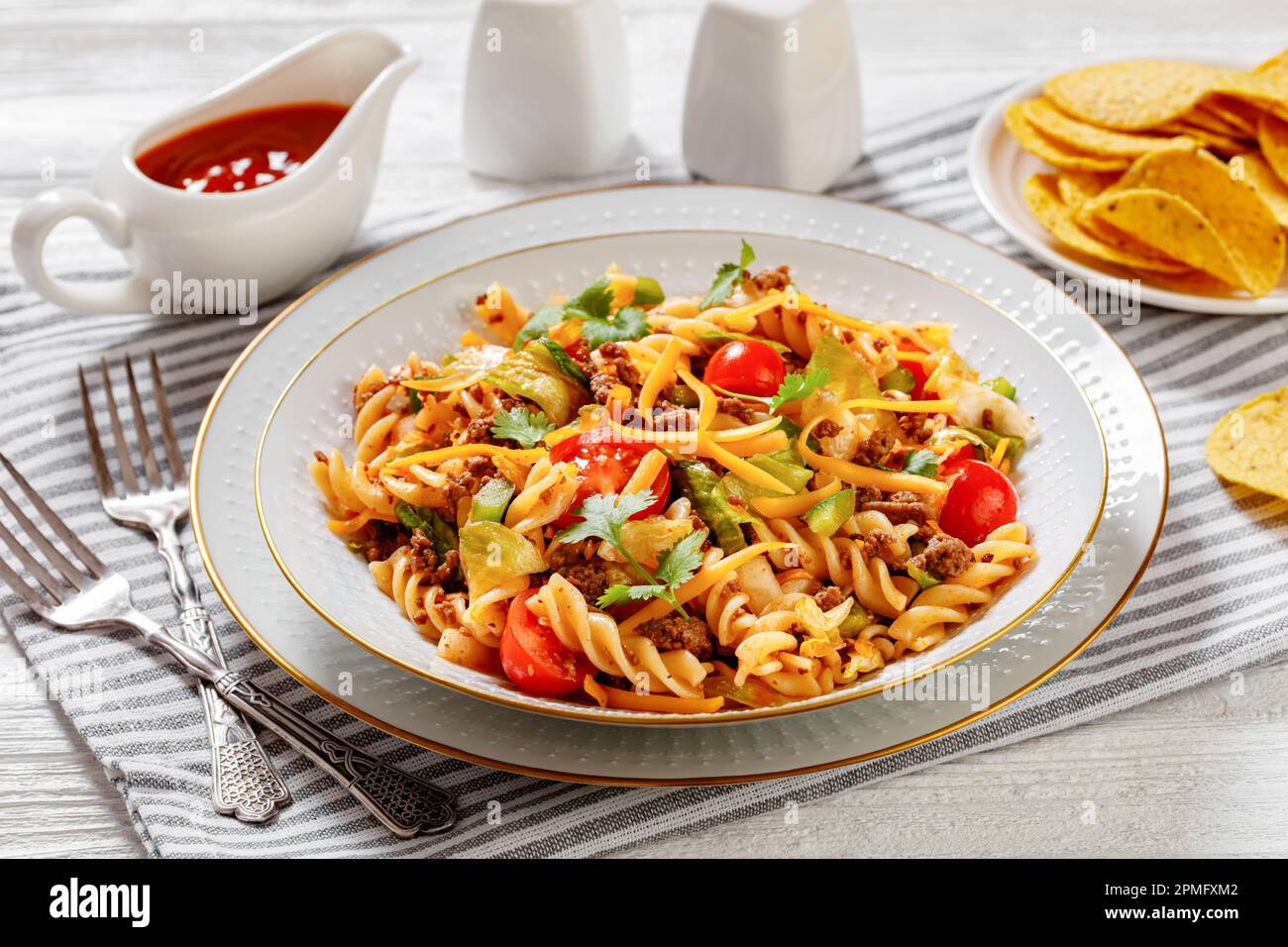 Insalata di pasta Nacho con carne macinata, pomodori, peperoni verdi, lattuga iceberg e condimento taco in ciotola bianca su tavola di legno bianco Foto Stock