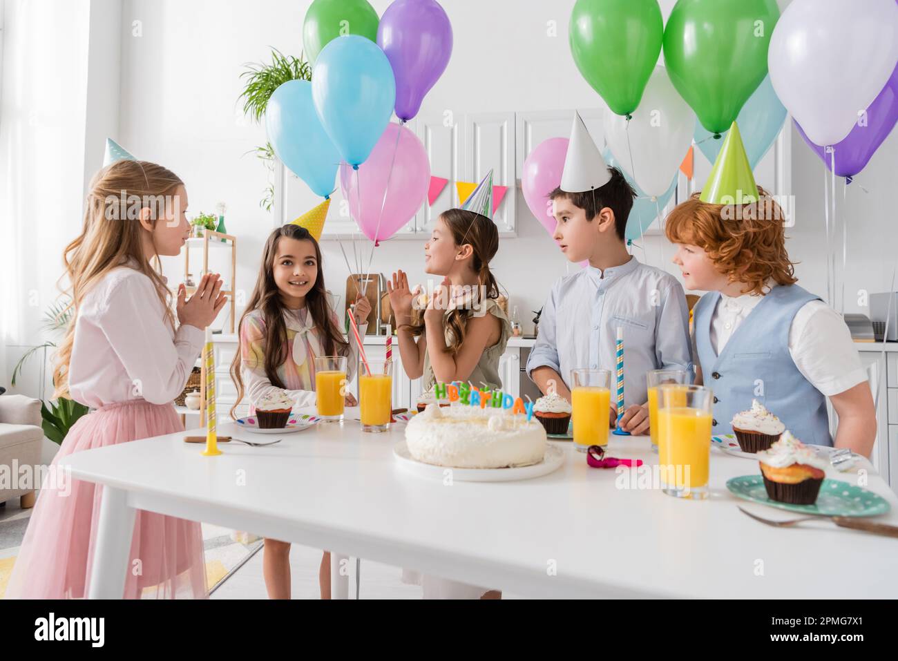 happy kids applapping mani e cantando felice canzone di compleanno accanto alla torta con candele e palloncini, immagine stock Foto Stock