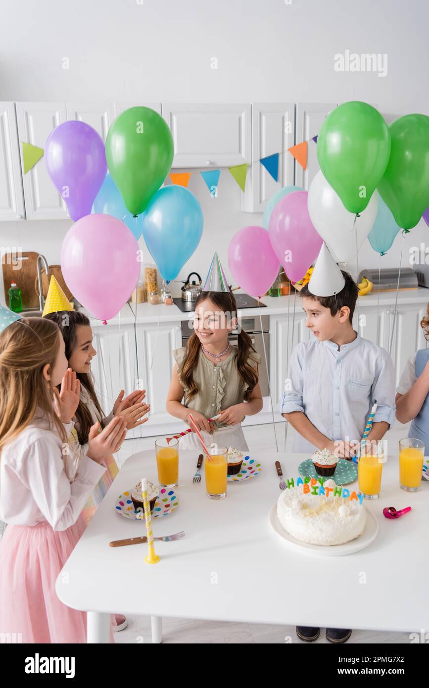 i bambini felici che battono le mani e cantano la canzone di compleanno felice vicino alla torta con le candele e i palloncini, immagine di scorta Foto Stock
