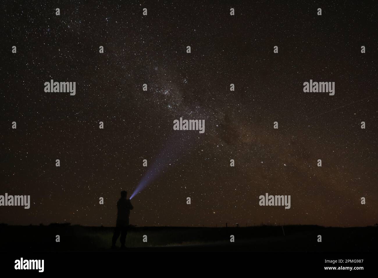 Una figura maschile è illuminata contro il cielo notturno, la sua silhouette raggiunge le stelle mentre afferra una sorgente luminosa luminosa in mano Foto Stock