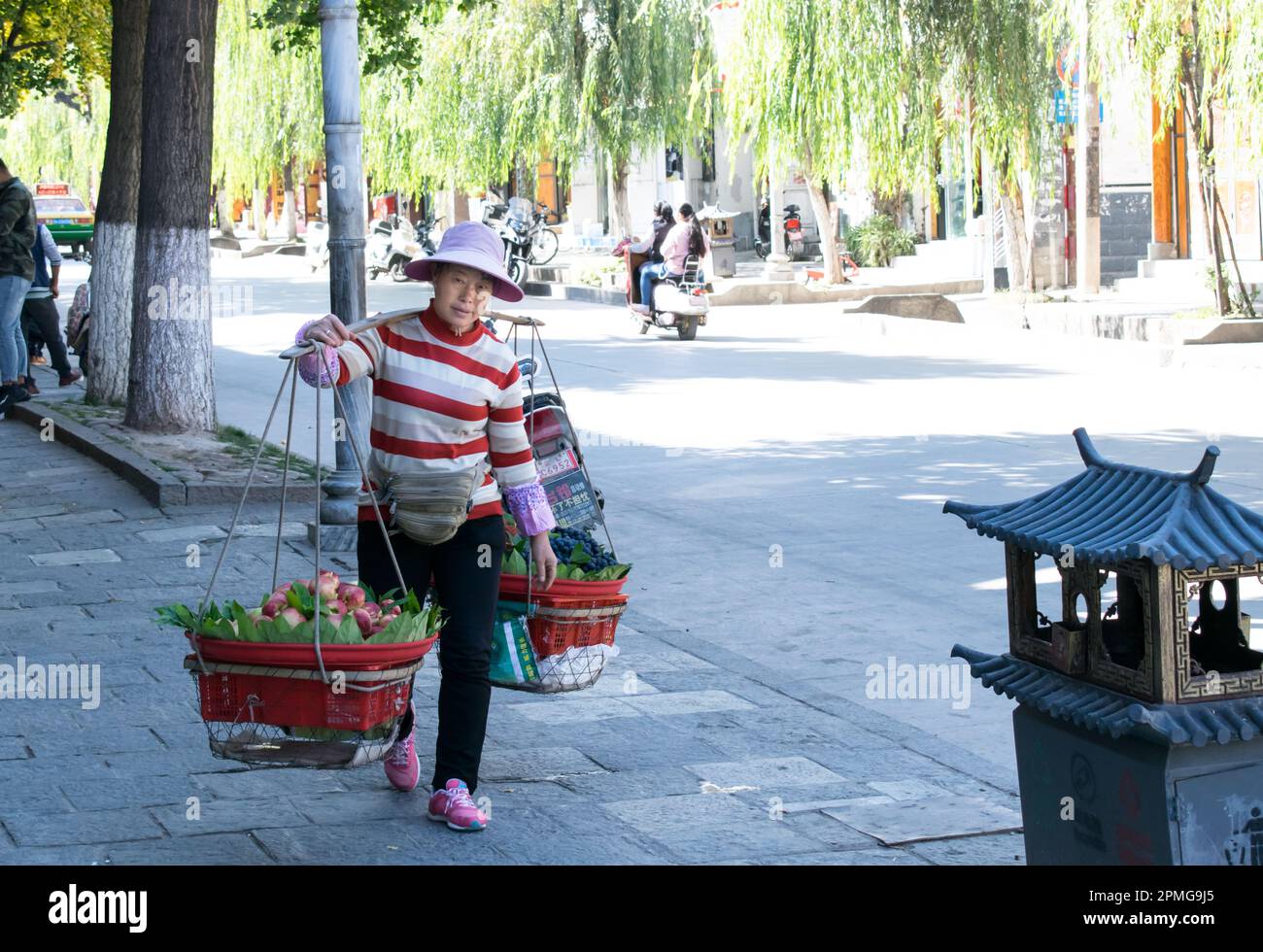 Una donna cinese trasporta la frutta per la vendita sui cestini appesi su un bastone sulle sue spalle - Dalí, Cina. Foto Stock