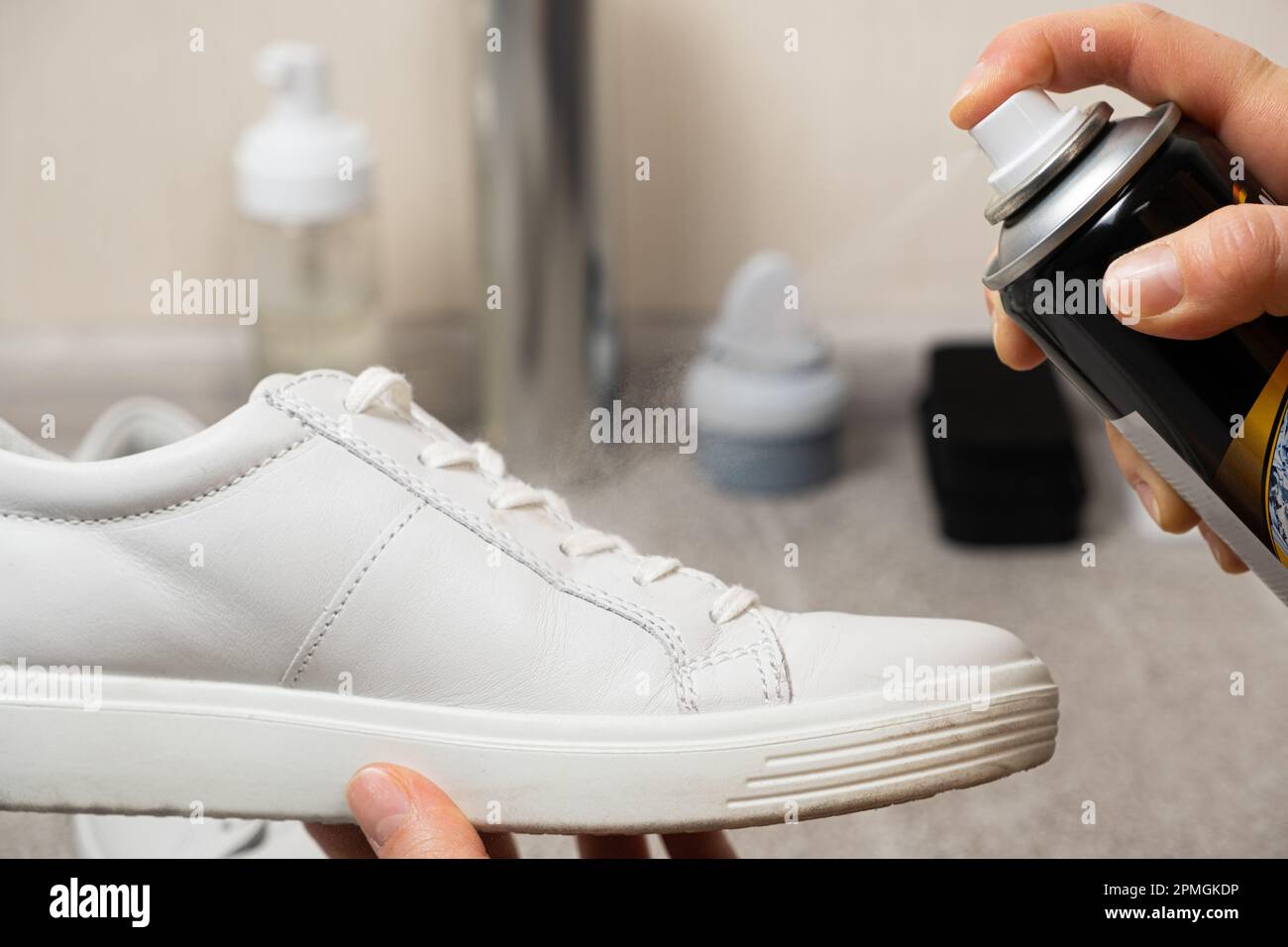 Applicare uno spray idrofobico idrorepellente alle sneaker bianche da donna. Protezione delle scarpe da umidità, sporco e odore sgradevole. Foto Stock