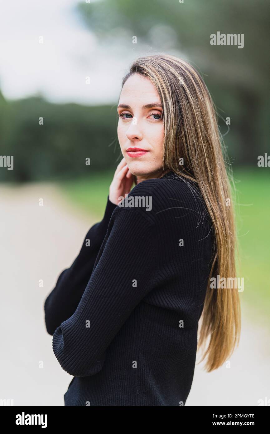 Una giovane donna in un maglione nero che guarda la telecamera con un lieve sorriso sul viso. Foto Stock