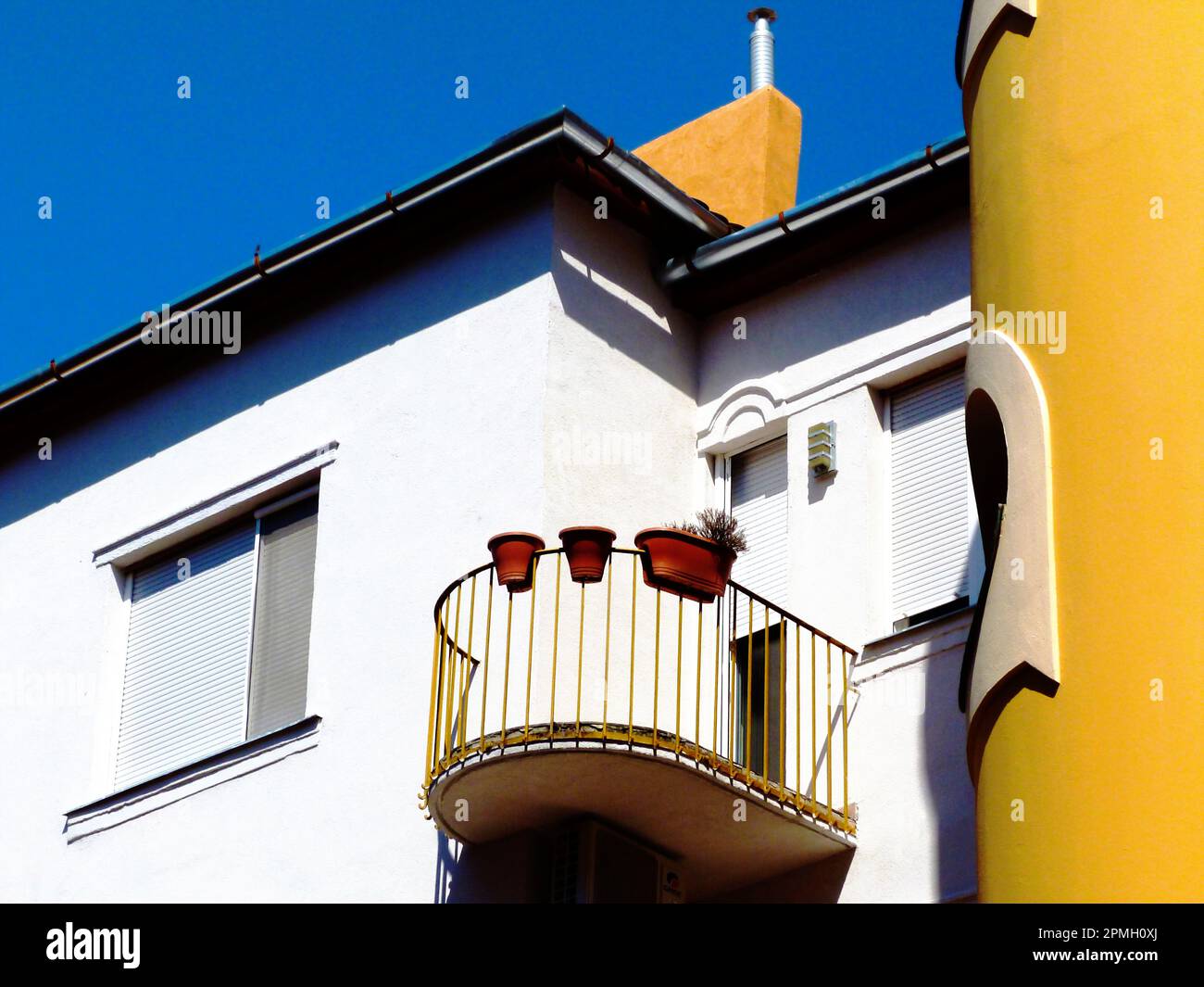 piccolo balcone di forma rotonda con ringhiera in metallo su vecchia facciata in stucco. vista ad angolo basso. vasi di fiori appesi sulla balaustra. cielo blu. vita urbana Foto Stock