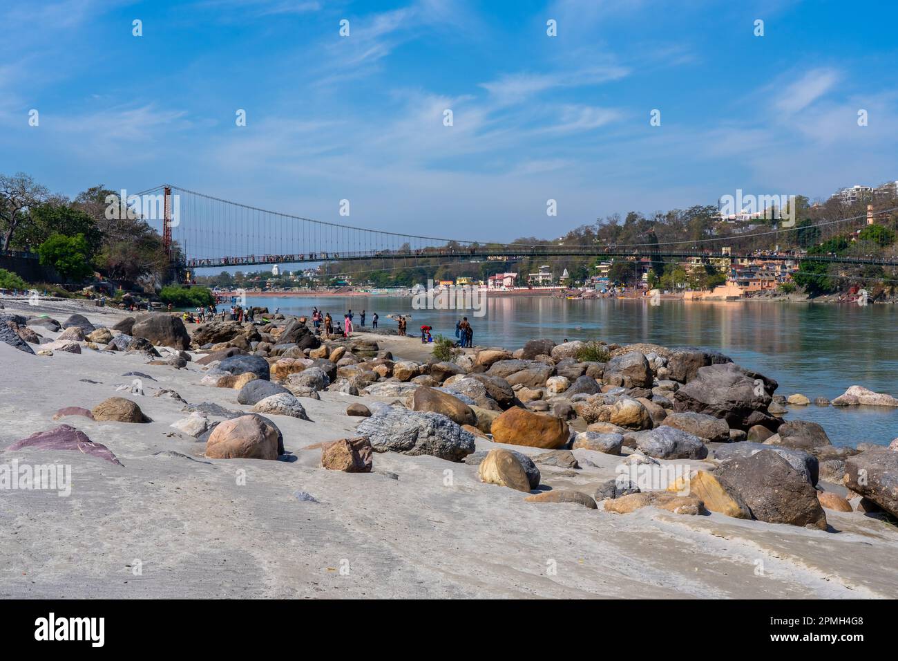 Rishikesh, Uttarakhand, India - 29.03.2023: Bel fiume Ganga a Rishikesh con la gente sulla spiaggia. Famoso ponte Lakshman Jhoola. Puro naturale Foto Stock