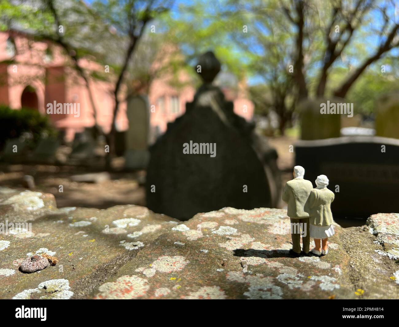 Concetto di perdita. I modelli di persone in miniatura raffigurano una coppia anziana dai capelli bianchi in piedi insieme in un cimitero. Foto Stock