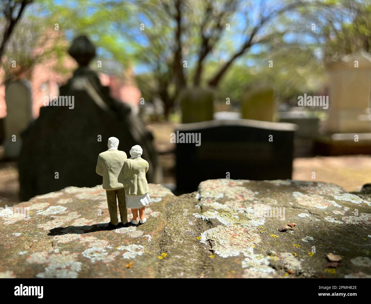 Concetto di perdita. I modelli di persone in miniatura raffigurano una coppia anziana dai capelli bianchi in piedi insieme in un cimitero. Foto Stock