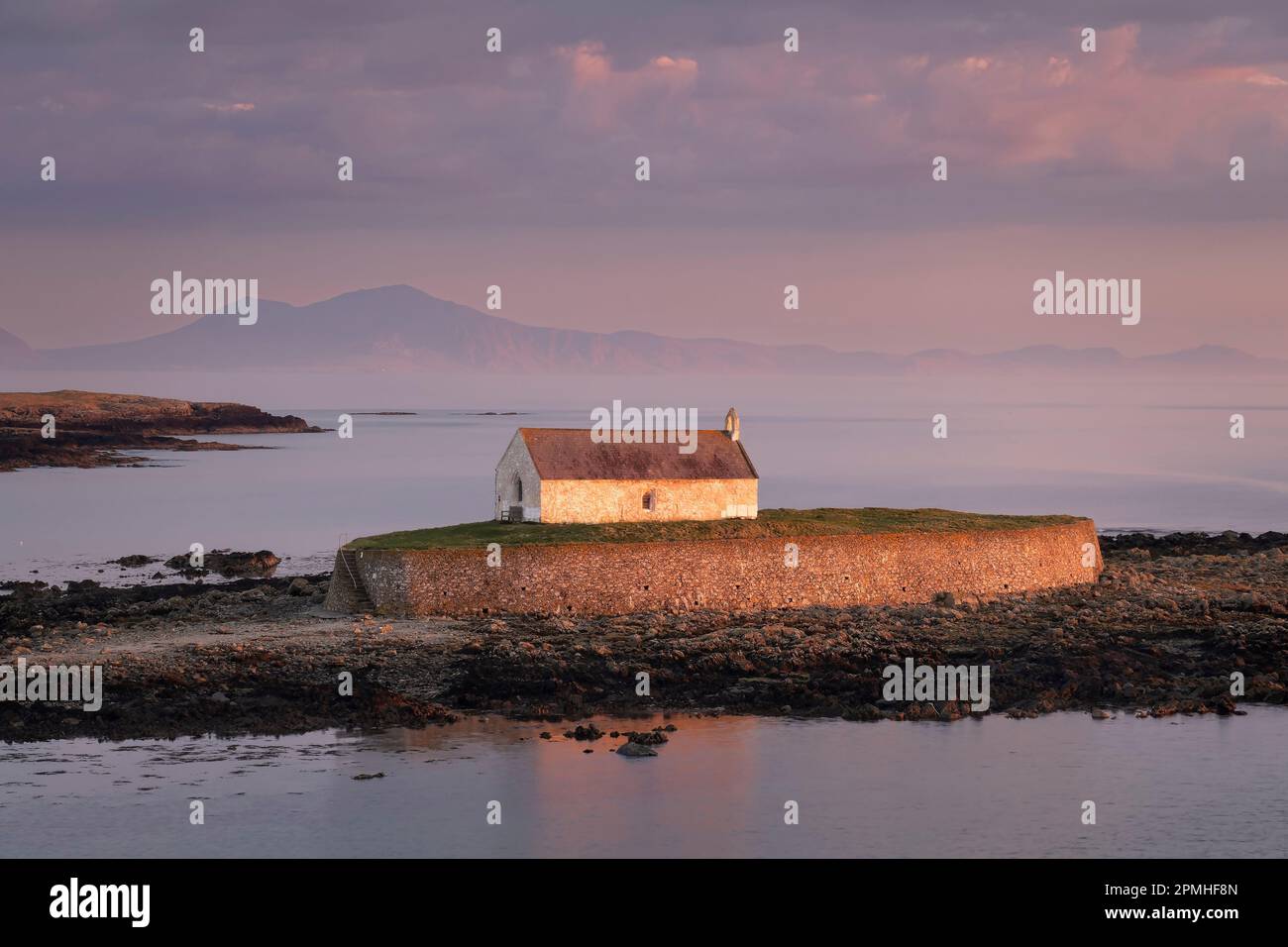 La luce serale illumina St. Cwyfan's Church (Chiesa nel mare) sull'isola di Cribinau sostenuta dalla penisola di Lleyn, vicino Aberffraw Foto Stock